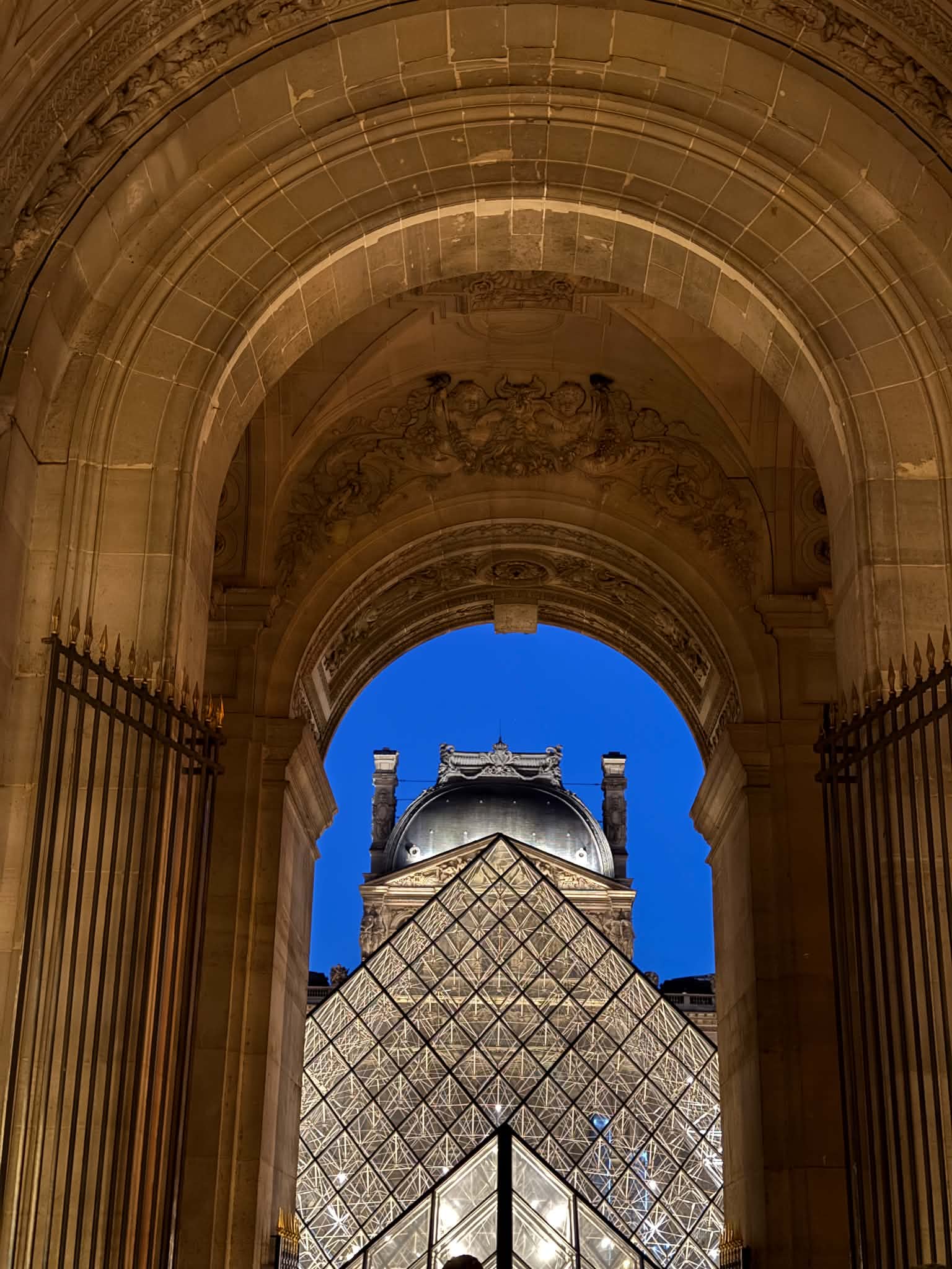 The Louvre Pyramid framed by an arch at blue hour
